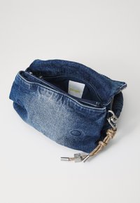 Denimová ramenní taška s měkkým, zmačkaným designem. Obsahuje horní zip, béžový uzlový popruh a označení značky uvnitř.