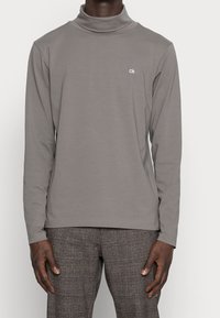 Graues langärmeliges Rollkragenshirt aus weichem Stoff, mit kleinem weißem "ck"-Logo auf der Brust und einem entspannten Schnitt.