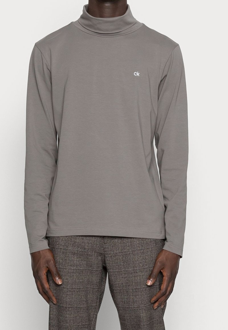 Graues langärmeliges Rollkragenshirt aus weichem Stoff, mit kleinem weißem "ck"-Logo auf der Brust und einem entspannten Schnitt.