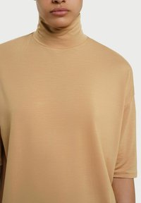 Beige turtleneck bluse med korte ærmer, der har en glat tekstur og en afslappet pasform. Stoffet virker let med en subtil glans.