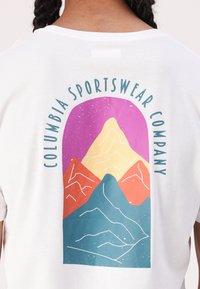 Camiseta de algodón blanca con un gráfico de montaña colorido que muestra montañas naranjas, amarillas y azules, rodeado del texto "Columbia Sportswear Company."