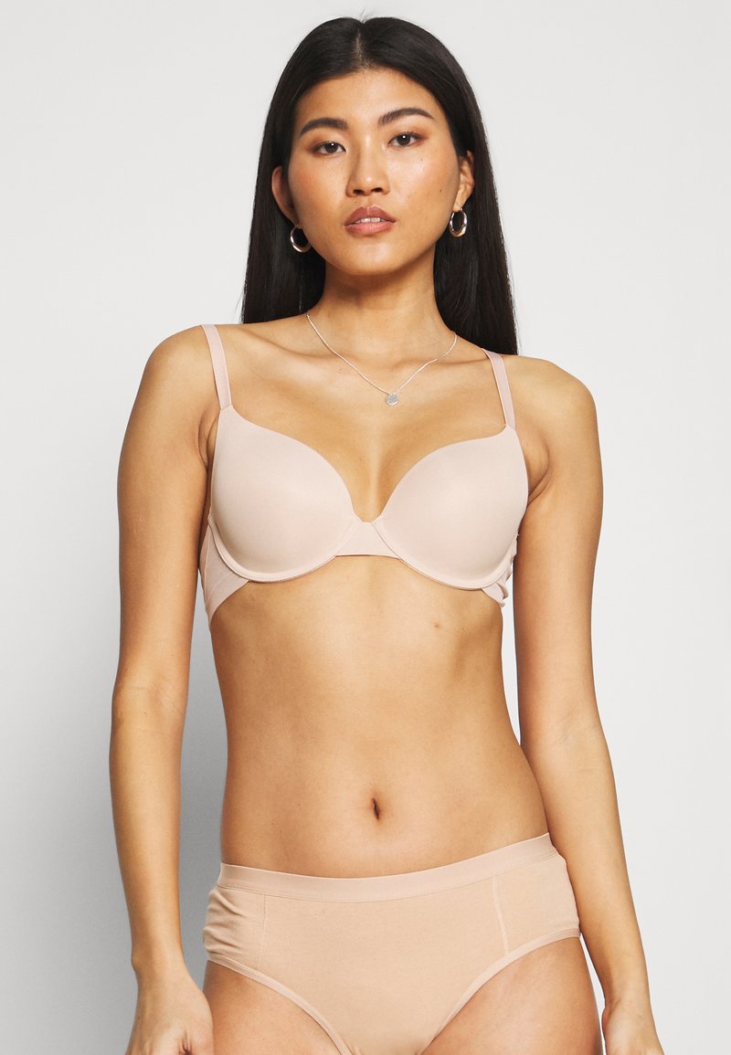 Molded bralette in light beige with adjustable straps and underwire support. Smooth texture with seamless design and a classic cup shape.