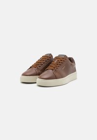 Ein Paar braune Leder-Sneaker mit flachem Schnitt, braunen Schnürsenkeln und weißen Gummisohlen, schräg auf einem weißen Hintergrund positioniert.
