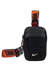Černá nylonová taška přes rameno s nastavitelným oranžovým popruhem, na kterém je logo "NIKE". Obsahuje zipovou kapsu a texturovaný povrch.