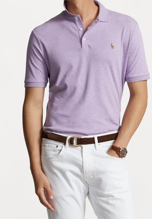 Lavendel polo skjorte med krave og tre knapper, parret med hvide bukser og et brunt bælte. Ur synligt på håndleddet.