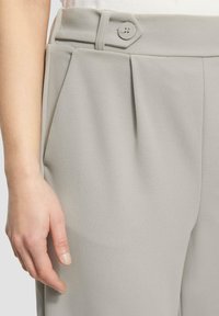 Graue maßgeschneiderte Hose mit hoher Taille, subtiler Textur, vorderen Falten und seitlichem Knopfverschluss.