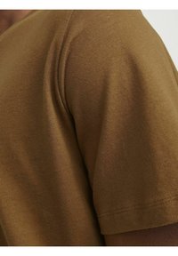 Brun bomulds t-shirt, rund halsudskæring, korte ærmer. Nærbillede, der viser den glatte tekstur og syningdetaljen ved ærmeenden.