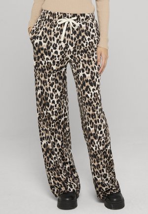 Woman wearing beige ribbed long-sleeve top and loose leopard print pants with white drawstring and black chunky shoes.