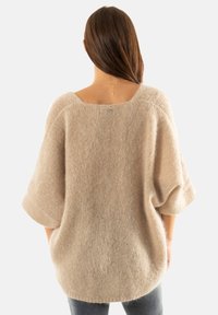 Pull en cachemire beige à manches courtes, texture tricotée, encolure large et petit détail en forme de cœur argenté à l'arrière.