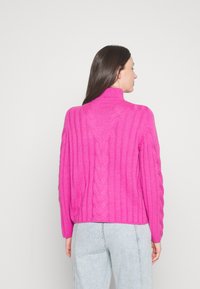 Fuksia värvi kudum, millel on vertikaalne soonik ja kaelus, mille tagaküljel on palmikute detail; omab kõrget kaelust ja veidi ülerohket lõiget.