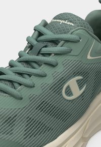 Πράσινο αθλητικό παπούτσι Champion από δίχτυ με κορδόνια, λογότυπο στο πλάι και μπεζ σόλα, εμφανιζόμενο σε κοντινή λήψη σε ελαφρύ πλάγιο προφίλ.