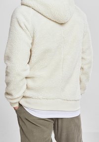 Hvid fluffy fleece hoodie med hætte, struktureret overflade og ribbede kanter. Båret over en hvid skjorte og parret med olivengrønne kordfløjlshorts.