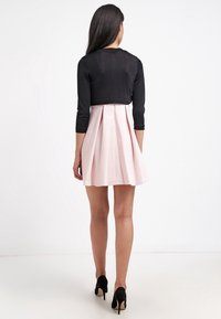 Svart, figurnära kort tröja med trekvartsärmar som är kombinerad med en ljusrosa, plisserad klänning. Tunn svarta klackskor fulländar outfiten.