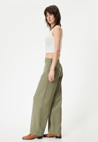 Oversized olijfgroene broek met een gladde textuur, met een hoge taille en elastische tailleband, gecombineerd met een aansluitend wit geribd tanktop.