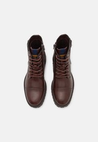 Botas de piel marrón hasta el tobillo con punta redonda, cordones en la parte delantera y cremallera lateral. Superficie texturizada y detalle azul en la lengüeta.