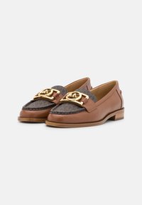 Bruine leren loafers met een donkergepatroneerd stof bovenop, afgewerkt met grote gouden metalen gespen, op een witte achtergrond.