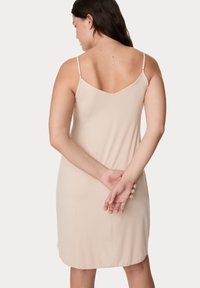 Vestido slip nude, de longitud a la altura de la rodilla, con tirantes delgados ajustables, espalda en forma de V, textura suave y sin patrones visibles ni herrajes.