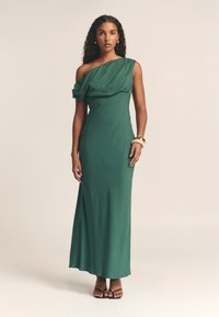 Zelena, maksi obleka z enim ramenom, izdelana iz gladkega blaga, ki se ponaša z draperijami na ramenu in prilegajočo silhueto. Preprost, eleganten dizajn.