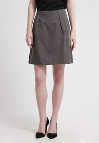 Jupe grise à mi-mollet avec des plis, en tissu texturé, et taille ajustée. Associée à des talons hauts noirs. Design simple et épuré.