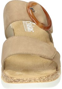 Sandale en suède beige avec un accent rond marron, deux larges brides, une ouverture à l'avant et une semelle intérieure texturée. Semelle en liège pour un confort supplémentaire.