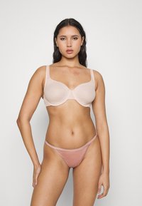 Lys rosa underwire-bh med ribbet tekstur og brede stropper, kombinert med matchende gjennomsiktig thong. Glatt finish og minimalistisk design.