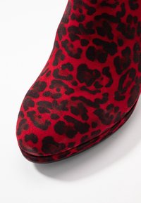 Bottine à imprimé léopard rouge avec une texture douce en daim, un bout arrondi et une semelle noire lisse et brillante.