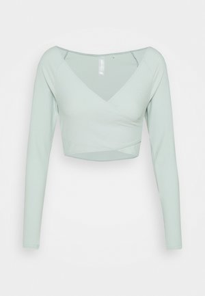 Haut court à manches longues côtelé vert clair, avec un décolleté en V profond et une silhouette ajustée.