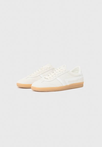 Baskets en suède blanc avec un design texturé, présentant une rayure plus claire et une semelle en caoutchouc gomme. Style lacé et low-cut avec un minimalisme dans les détails.