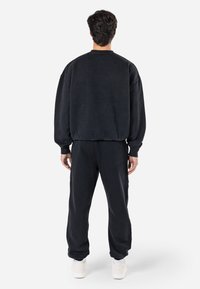 Sort bomulds-sweatshirt med drop-shoulders og ribbede manchetter, parret med matcherende sweatpants. Enkel design, afslappet pasform og struktureret stof.