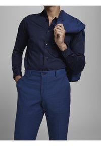 Námořnická košile s úzkým střihem a límcem na knoflíky, v kombinaci s přizpůsobenými modrými kalhotami. Odpovídající sako oblíbené přes rameno.