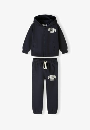 Sötétkék kapucnis pulóver és melegítőnadrág szett, elől cipzárral, két zsebbel és fehér hímzéssel a "OREGON 1997" felirattal mindkét darabon.