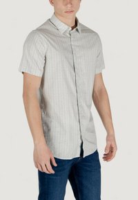 Camicia a maniche corte con bottoni di colore grigio chiaro, con un sottile motivo geometrico, dotata di colletto classico e vestibilità comoda, abbinata a jeans blu.