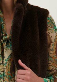 Faux fur stole in donkerbruin, met een zachte textuur. Gecombineerd met een gestreepte groen en gouden blouse, die ingewikkelde ontwerpen toont.