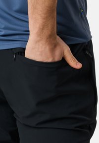Zwarte sportbroek met zijzakken, gedragen met een blauwe geperforeerde shirt. Duidelijke ritszakdetails op de broek.