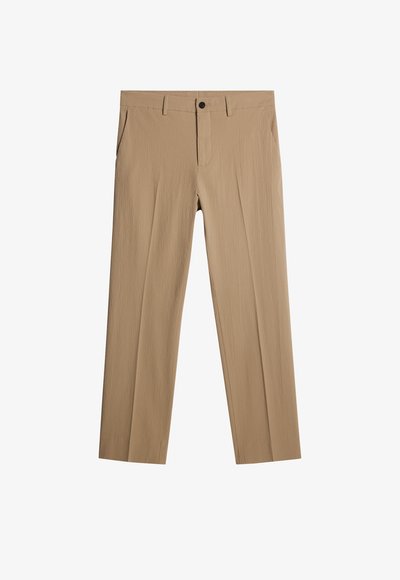 Beżowe spodnie z fakturowanej tkaniny o luźnym kroju. Posiadają zapięcie na guzik z przodu, kieszenie boczne i brak widocznych wzorów.