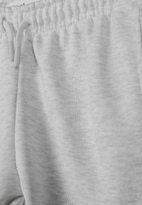 Pantalon de jogging gris clair avec ceinture élastique et cordons blancs, montrant la texture douce du coton et la couture de la poche latérale.