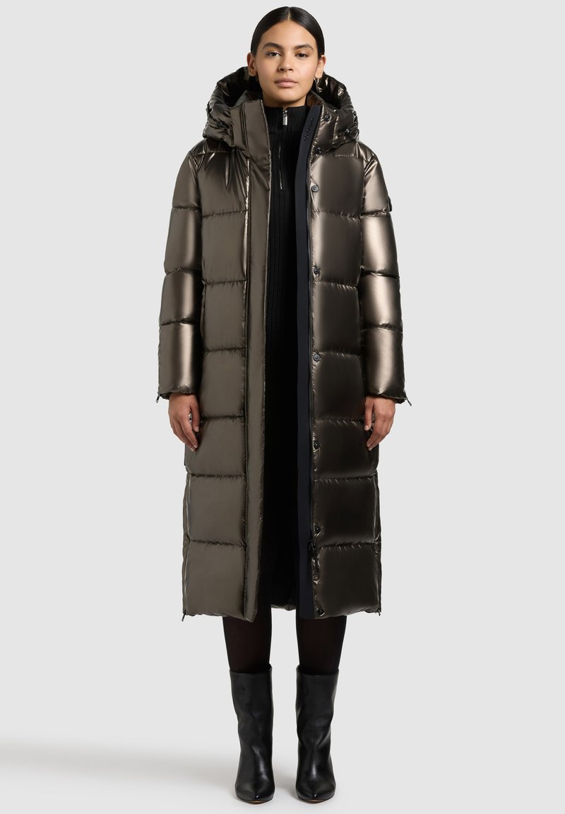 Metallischer, knielanger Puffermantel mit Kapuze; gestepptes Design; glänzende Textur; Frontknöpfe; schwarze Akzente; kombiniert mit schwarzen Stiefeletten.