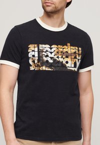 Camiseta de algodón negra con estilo ajustado y cuello acanalado de color crema. Presenta un diseño gráfico en capas y con textura en naranja y blanco.