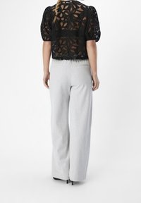 Haut court en dentelle noire avec manches bouffantes et motif floral ; associé à un pantalon large taille haute gris clair.