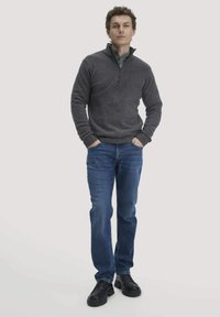 Grauer Fleece-Pullover mit einem Reißverschlusskragen, kombiniert mit blauen Jeans und schwarzen Schuhen. Der Pullover hat eine weiche Struktur und ribbelige Bündchen.