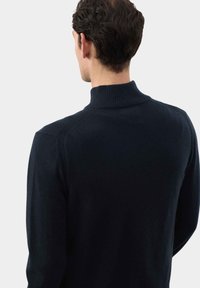 Maglione a maglia blu navy con colletto alto a coste e maniche lunghe, caratterizzato da una texture liscia e un design aderente per un look moderno.