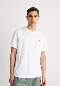 White cotton T-shirt featuring a round neckline, short sleeves, and a small colorful logo on the left chest area. Smooth texture.