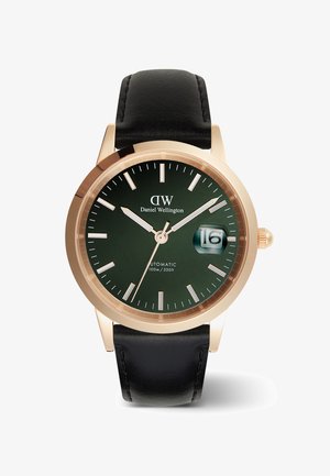 Orologio automatico rotondo con quadrante verde scuro, indicatori delle ore color oro e funzione data. Presenta un cinturino in pelle nera e cassa dorata.