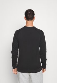 Sudadera negra de manga larga con puños de canalé. Presenta un cuello redondo y un diseño sencillo, combinada con pantalones gris claro.