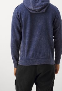 Granatowy bawełniany hoodie o teksturowanym wykończeniu, z kapturem ze sznurkiem i ściągaczami przy mankietach. Z luźnym krojem.