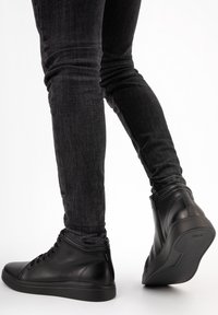 Černé vysoké tenisky vyrobené z hladké kůže, s texturovanou podešví, šněrováním a kontrastními stehmi.