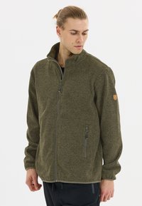 Olivgrön fleecejacka med hög krage, frontdragkedja och två sidofickor. Texturerat tyg med ett emblem på vänster axel.