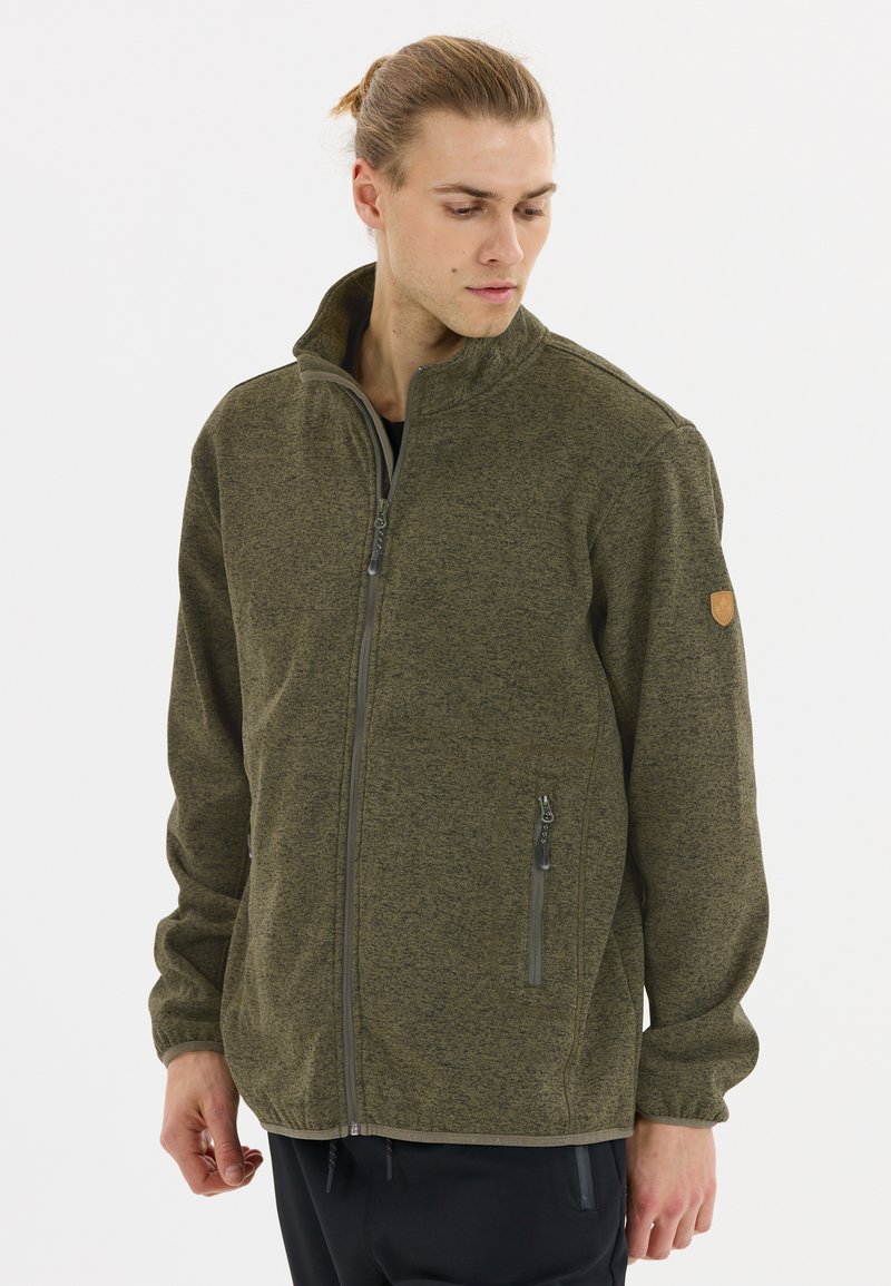 Olivgrön fleecejacka med hög krage, frontdragkedja och två sidofickor. Texturerat tyg med ett emblem på vänster axel.