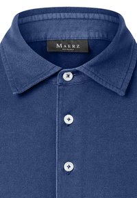 Niebieska polo z fakturą, z szerokim kołnierzykiem i trzema białymi guzikami, z czarną metką Maerz Muenchen wewnątrz kołnierza.