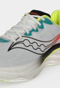 Λευκό αθλητικό παπούτσι Saucony με τιρκουάζ και κίτρινες λεπτομέρειες, λευκά κορδόνια και μαύρο λογότυπο στο πλάι, που δείχνει την μπροστινή και πλαϊνή όψη.